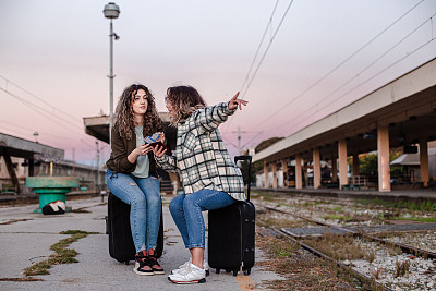 一群年轻的女孩坐在他们的行李上，指指点点地指着火车。火车站里的旅客