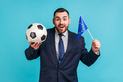 兴奋的男子穿着官方风格的西装，手持黑白足球和欧盟旗帜，观看足球和支持喜爱的球队。