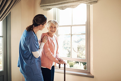 一名年轻护士和一名老年妇女站在养老院的窗户旁