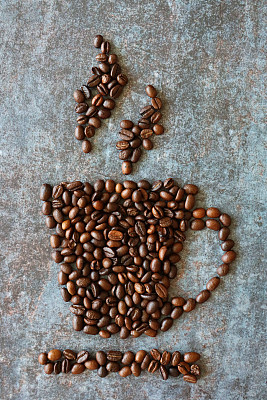 咖啡杯和咖啡碟的图像与上升的蒸汽设计形成了一堆烤咖啡豆，斑驳的，灰色的背景，升高的视野