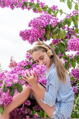 可爱的少女戴着耳机在舒适的阳台上享受着美丽的粉色九重葛