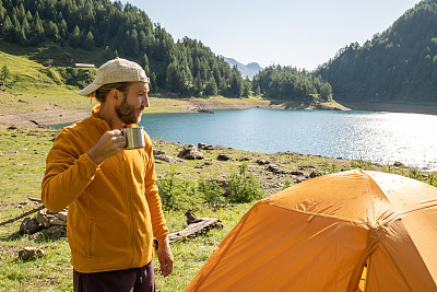 早上，一个男人在他的帐篷旁喝咖啡
