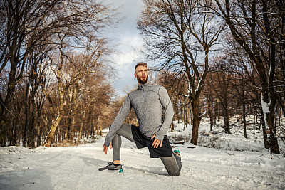 身体健康的运动员在雪天跪在大自然中做热身和伸展运动。冬季健身，健康生活方式