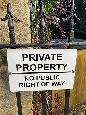 白色和黑色的标志在金属栅栏的大门上，提示“私人财产，没有公共通行权”，重点在前景