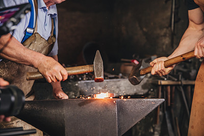 两个铁匠在铁砧上敲打铁锤在热金属件上的中部