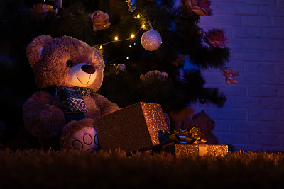 圣诞树下的泰迪熊和打开的礼物盒。