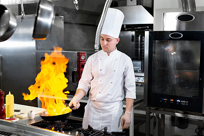厨师在厨房炉灶上的煎锅中用火焰烹饪