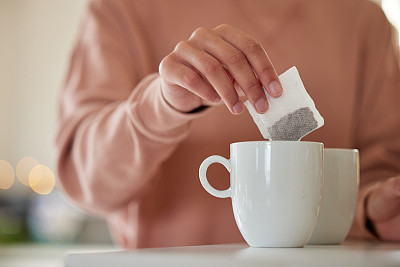 一个女人把一个茶包扔进一个等待着的杯子里