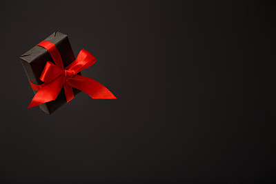 美丽的飞行黑色礼盒与红色蝴蝶结在黑色的背景。黑色星期五促销，圣诞节促销，折扣概念。情人节。父亲节
