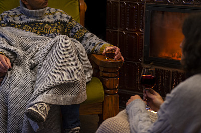 这是一个轻松舒适的夜晚，这对中年夫妇穿着暖和的毛衣，裹着针织毯子坐在壁炉边，手里拿着一杯酒，气氛舒适，很低调