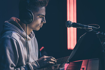 年轻人戴着耳机，拿着笔记本电脑，在音乐键后面。