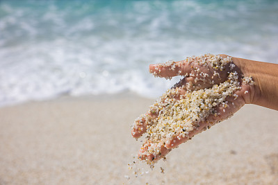 在意大利撒丁岛的海滩上，女人的手在玩沙。
