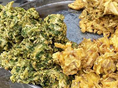 全帧图像，一堆酥脆的洋葱bhajis和palak pakora(菠菜馅饼)上的不锈钢塔利(托盘)，印度街头美食素食小吃，高架视图，重点在前景