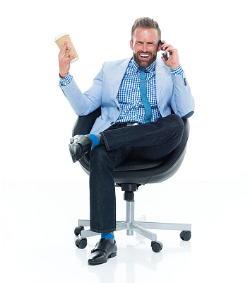 白人年轻男性商人，打着领带坐在白色背景前面，拿着咖啡杯，用手机