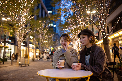 年轻的女性朋友在圣诞灯光下的街头咖啡馆里喝咖啡