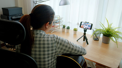 亚洲自由职业妇女演奏吉他与乐队通过视频会议音乐应用程序，而呆在家里。