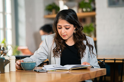 年轻的女商人在咖啡馆里看书喝咖啡。
