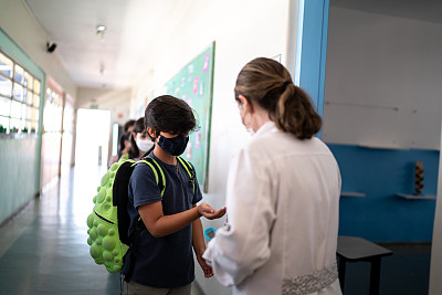 老师在学生进教室前，使用口罩在学生手上涂抹洗手液