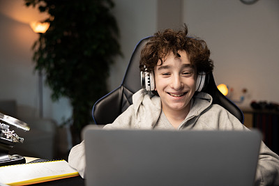 快乐的聪明的小男孩的肖像在笔记本电脑的网络摄像头微笑。孩子可以远程上课，和老师视频聊天。他正在使用无线耳机