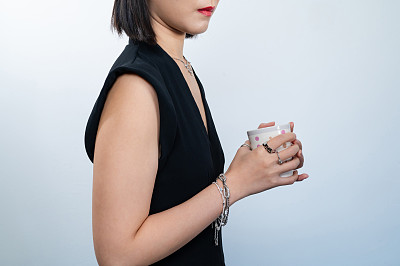 这是一个女人拿着一杯咖啡，用白色的背景装饰着钻石戒指和银手镯等奢侈品