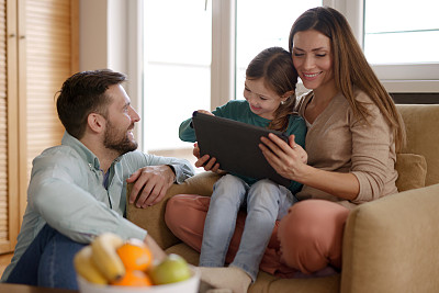 快乐的父母和他们的女儿在家里使用数码平板电脑