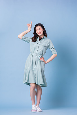 年轻的亚洲妇女穿着蓝色背景的连衣裙的全长图像