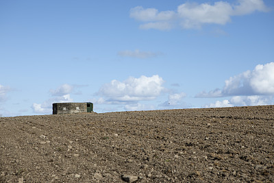 蓝色多云的天空下，一片耕地的地平线上有碉堡式的防空洞