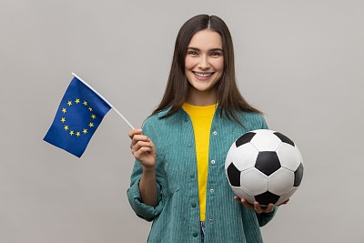 女子手持黑白相间的足球和欧盟国旗，观看足球比赛，支持自己喜欢的球队。
