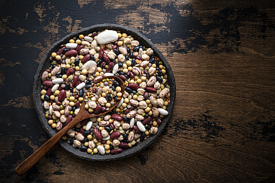混合干豆类在一个盘子与勺子在质朴的深色木制背景