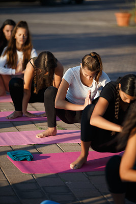 一群年轻女性蹲在户外的瑜伽垫上，双手紧握