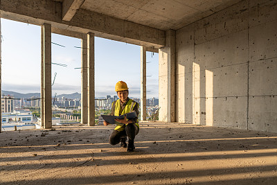 阳光透过建筑工地，一名女工程师蹲在地上拿着文件夹查看数据