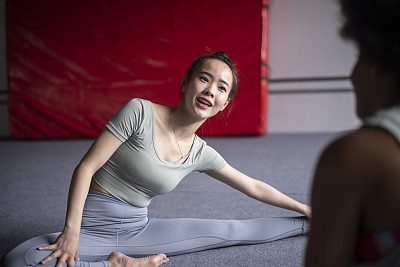 亚裔中国女人在健身房伸展时微笑和聊天的中景