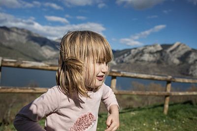 小女孩开心地笑着，风吹着她的头发在美丽的自然景观。