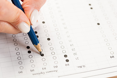 学生们手拿考试，用铅笔在考场的光学形式的标准化考试上写字，答案和一张英语纸放在排椅上，在教室里做期末考试。