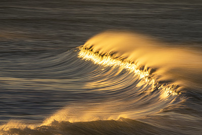 清澈的海浪在沙滩上反射出明亮的金色日出