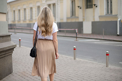 一个穿着白色t恤和裙子的金发女孩在城市里散步的背影