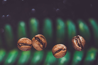 咖啡豆在闪亮的黑色背景下的特写。咖啡豆在绿叶背景。咖啡的背景。用咖啡豆复制空间。咖啡豆放在餐桌上。咖啡豆的特写