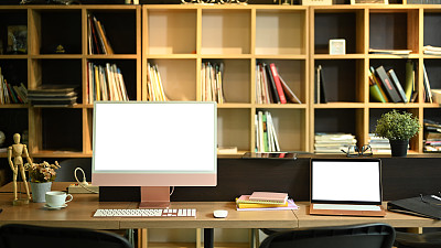 现代化的工作场所，配备电脑pc，笔记本电脑，咖啡杯和办公用品的木桌。广告文本的空屏幕。