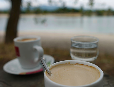 选择性对焦拍摄的一杯咖啡在一个湖岸边的餐厅的木桌
