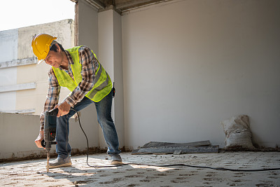 建筑工人在施工现场使用电动手提钻打孔设备，在浇筑地面前打孔，使地面坚固，工人和住宅建筑的概念。