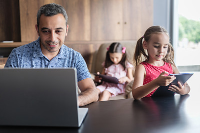 孩子和父亲在家里使用笔记本电脑和数字平板电脑，跨设备组概念