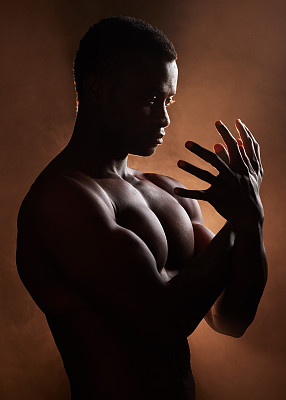 一个英俊，肌肉发达的年轻非洲裔美国人在演播室的黑暗背景。一个穿着黑色衣服，看起来若有所思的男性运动员。锻炼身体和思想。心理健康问题