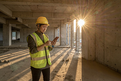 一位亚洲女建筑工人正在工地上使用手机