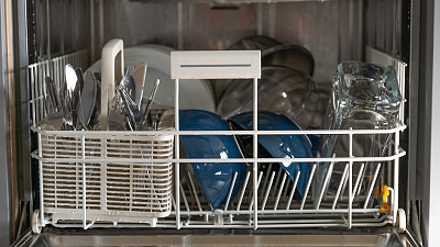 有干净盘子的洗碗机。厨房电器。盘子，叉子和杯子在洗碗机里。