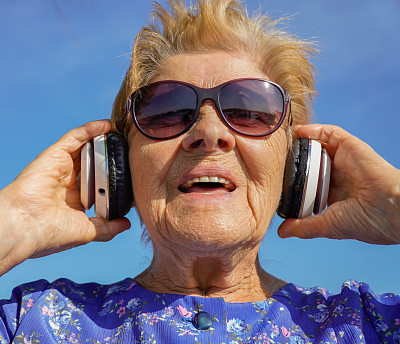 退休妇女戴着耳机听音乐笑。神经疗法