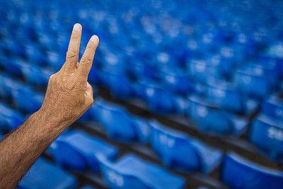 一名老人在一排排蓝色椅子后面举着一个和平手势
