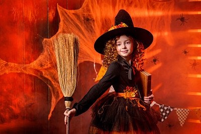 万圣节快乐。可爱开朗的小女巫与咒语书和扫帚。