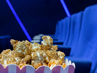 近距离图像的纸箱爆米花在电影院电影院座位，电影零食食品浴缸，蓝色天鹅绒座椅，重点在前景