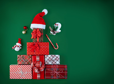 圣诞绿色背景。圣诞树形状的礼品盒，顶部有圣诞老人的帽子。