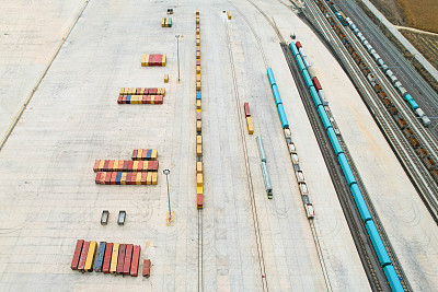 无人机视角下，物流中心的运输集装箱排成一排，火车轨道在其一侧